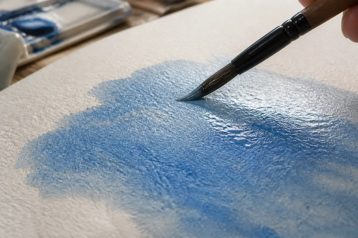 Aquarelle en cours, glacis bleuté posé sur un papier grain torchon avec pinceau chargé d&rsquo;eau